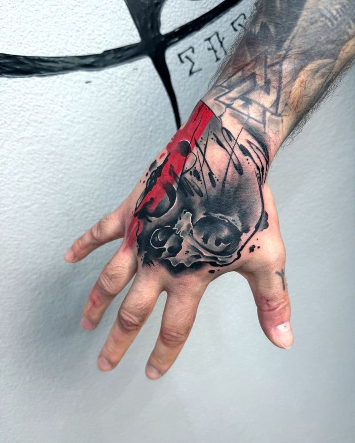 Trash-Aquarell-Tattoo mit roten Pinselflächen und Schädel auf dem Handrücken